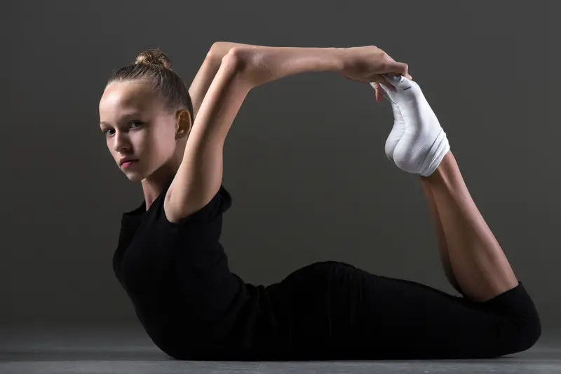 A rhythmic gymnast performing a deep stretch, focusing on flexibility and mobility as part of her training routine.